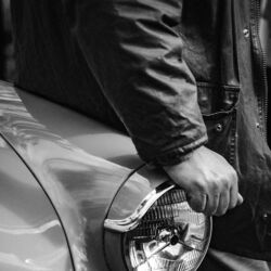 A hand rests on the headlight of an old car
